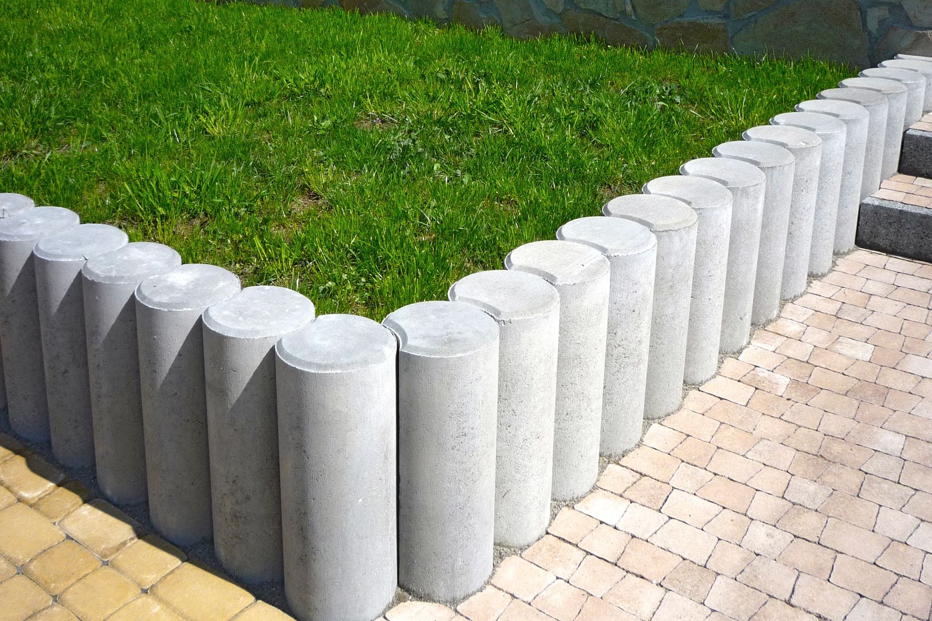 Turf lawn edged with round concrete bollards beside a paver path